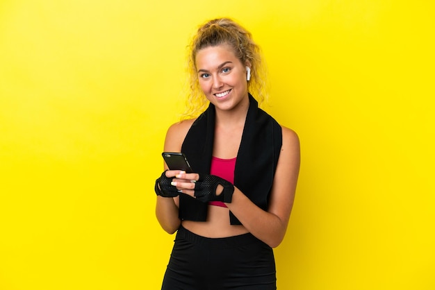 Femme sportive avec une serviette isolée sur fond jaune envoyant un message avec le mobile