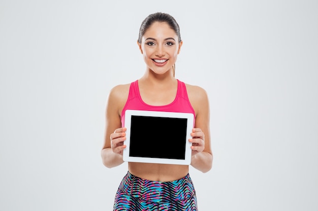 Femme sportive souriante montrant un écran d'ordinateur tablette vierge