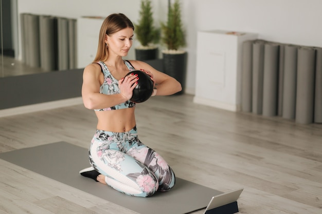 Une femme sportive en tenue de sport fait des exercices à la maison. Femme regarde dans la tablette pendant les exercices de diong.