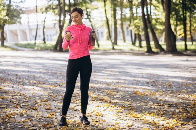 Femme sportive utilisant le téléphone et l'eau potable dans le parc