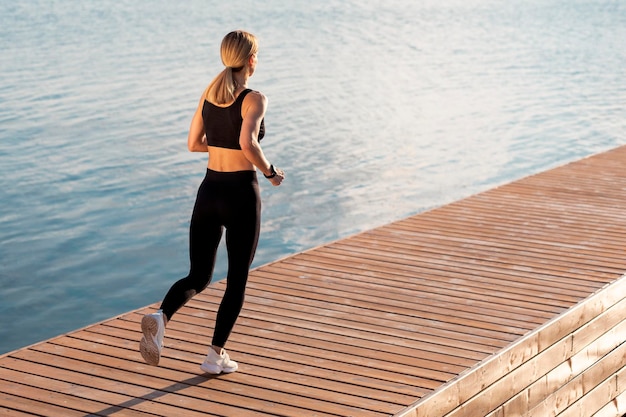 Femme sportive en vêtements de sport courant à l'extérieur sur une jetée en bois près de la rivière