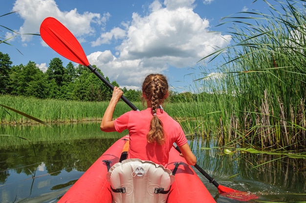 Une femme sportive vêtue de vêtements clairs rame un kayak rouge le long de la rivière Zdvizh. Ukraine