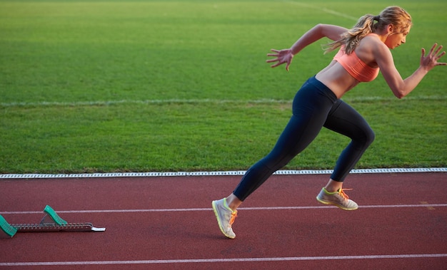 Photo femme sprinter laissant des blocs de départ sur la piste d'athlétisme. vue de côté. début explosif