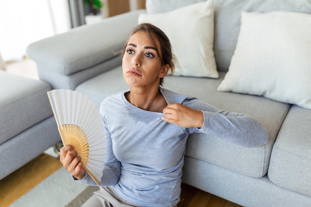 Une femme stressée et agacée utilisant un ventilateur agitant souffre d'une surchauffe de la chaleur estivale problème d'hormone de santé la sueur de la femme se sent mal à l'aise chaud en été problème de temps sans climatiseur