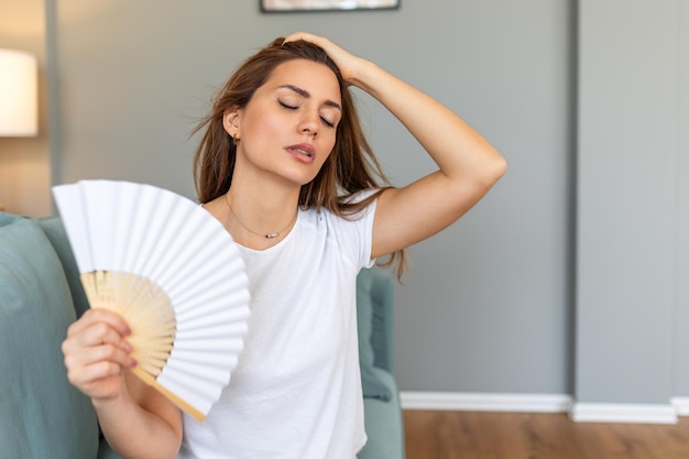 Femme stressée, agacée, utilisant un ventilateur ondulant, souffre de surchauffe, chaleur estivale, problème hormonal de santé, femme qui transpire, se sent mal à l'aise, chaleur en été, problème météorologique sans climatiseur.