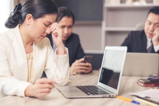 Une femme stressée est assise à son bureau au bureau Après une longue période d'utilisation d'un ordinateur portable, une femme d'affaires fatiguée enlève ses lunettes souffrant de fatigue oculaire et du syndrome des yeux secs