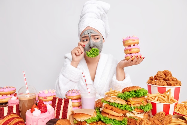 Une femme stressée et fatiguée de suivre un régime déteste manger de la verdure essuie des larmes en regardant de la malbouffe appétissante