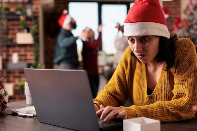 Femme stressée irritée travaillant dans un bureau bruyant, se sentant dérangée par des collègues sur un lieu de travail décoré d'ornements de vacances festifs. Personne surmenée fatiguée dans l'espace de l'entreprise.