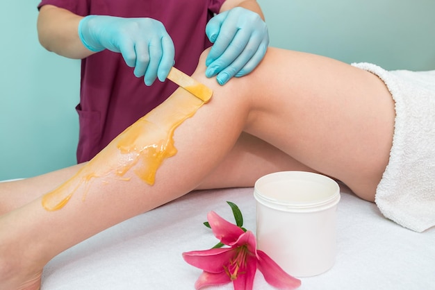 Photo femme subissant une procédure d'épilation des jambes avec de la pâte à sucre dans le salon soins de la peau enlever les cheveux avec de la pâte à sucre