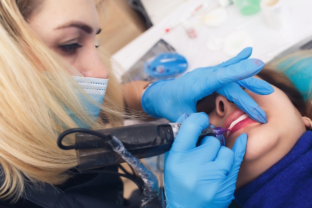 Une femme subit une procédure permanente de maquillage des lèvres dans un salon de tatouage