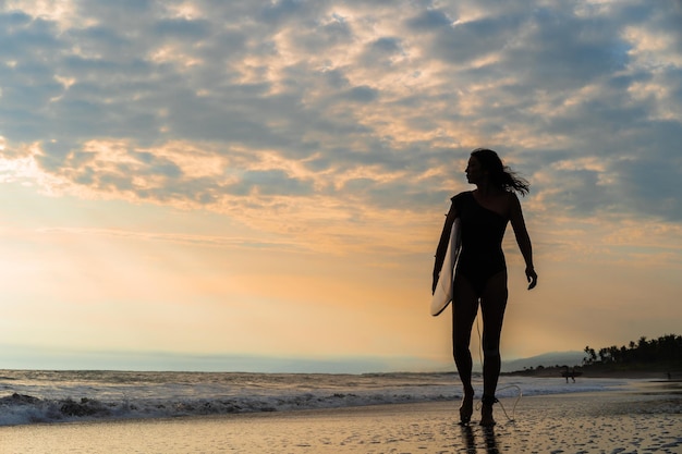 Femme surfeur avec planche de surf sur l'océan au coucher du soleil