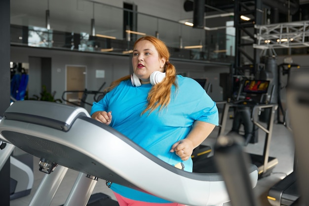 Femme en surpoids active qui court sur un tapis roulant et fait de l'exercice cardio pour brûler des calories. Défi sportif pour perdre du poids