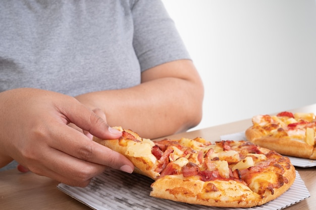 Femme en surpoids affamée tenant une pizza et heureuse de manger de la pizza.