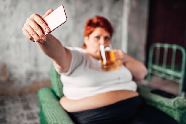 Une femme en surpoids boit de la bière et fait des selfies, de la paresse et de l'obésité. Mode de vie malsain, femme grasse