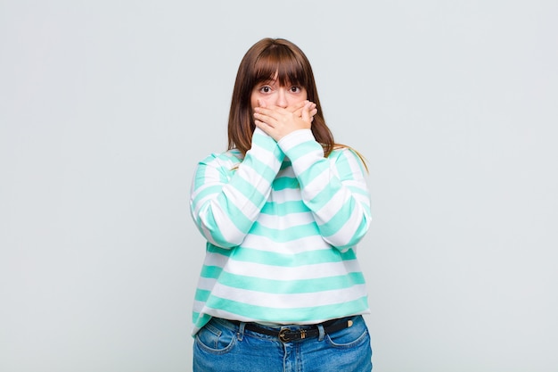 Femme en surpoids couvrant la bouche avec les mains avec une expression choquée et surprise, en gardant un secret ou en disant oups