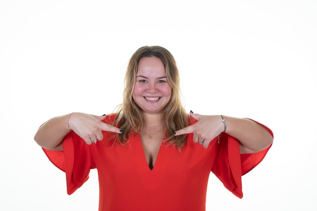 Femme en surpoids curvy portrait blonde à la fière positive et décontractée pointant vers la poitrine rouge avec les mains des doigts sur fond blanc