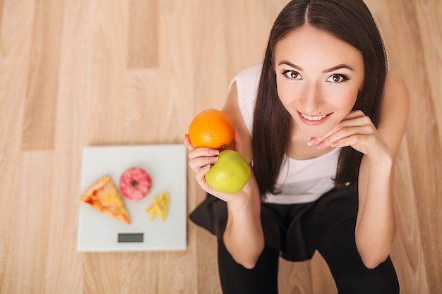 Femme en surpoids debout sur une balance tenant une pizza.