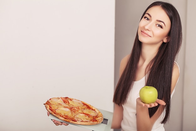 Femme en surpoids debout sur une balance tenant une pizza.