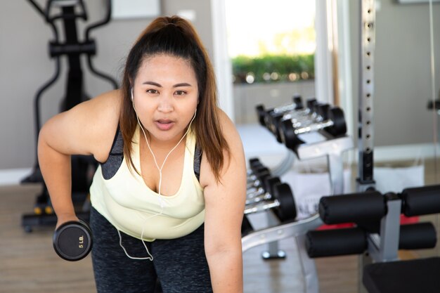 Femme en surpoids faisant une séance d'entraînement de remise en forme avec des poids au gymnase.