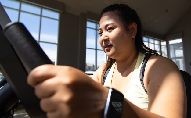 Femme en surpoids faisant une séance d'entraînement de remise en forme à vélo au gymnase. Concepts de mode de vie sain et de sport.