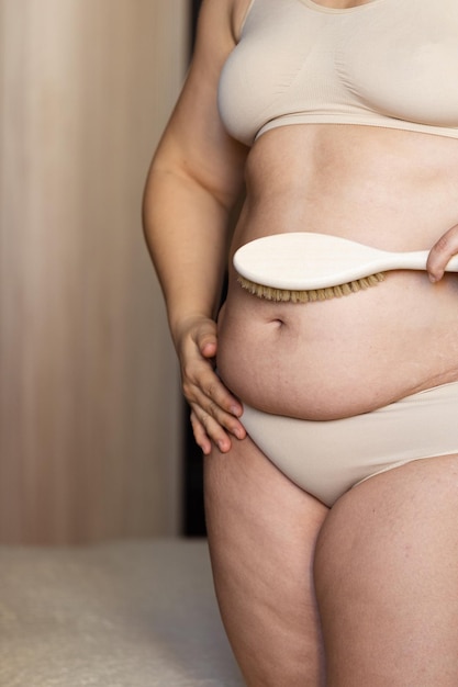 Femme en surpoids recadrée en sous-vêtements poids excessif graisse ventre brosse massage sec soins du corps cellulite
