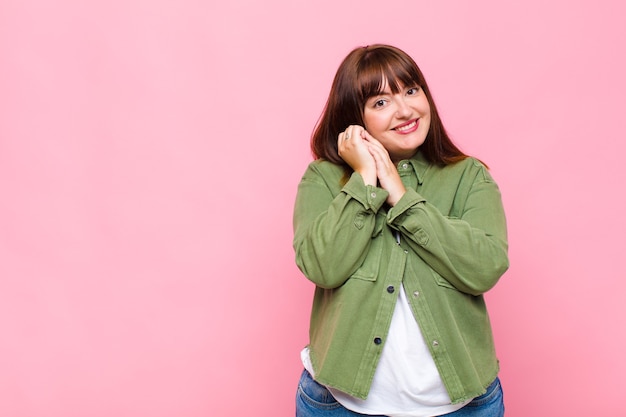 Femme en surpoids se sentant amoureuse et à la recherche de mignon, adorable et heureux, souriant romantiquement avec les mains à côté du visage