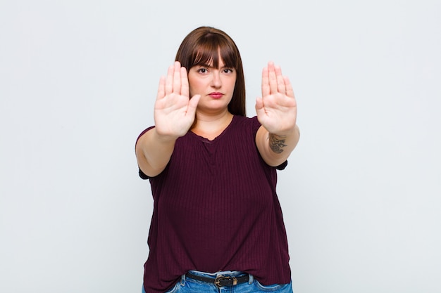 Femme en surpoids à la sérieuse, malheureuse, en colère et mécontente d'interdire l'entrée ou de dire arrêter avec les deux paumes ouvertes