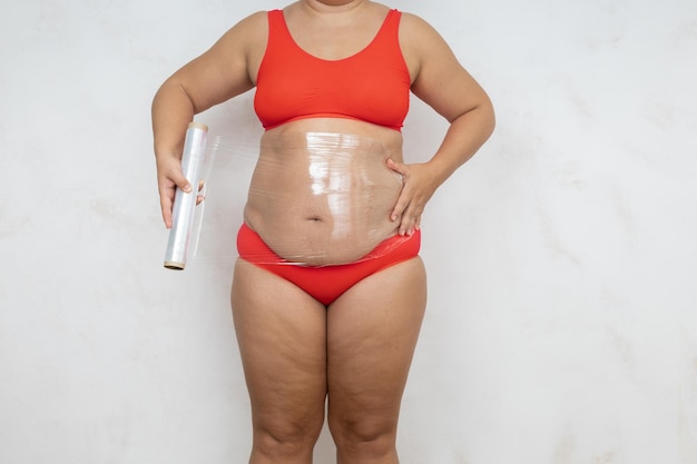 Photo femme en surpoids wrap ventre avec film alimentaire fond blanc femme nue en sous-vêtements rouges avec grand