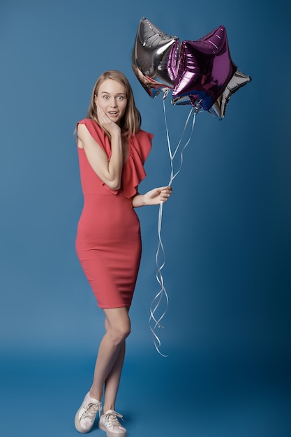 Femme surprise avec des ballons étoiles sur mur bleu