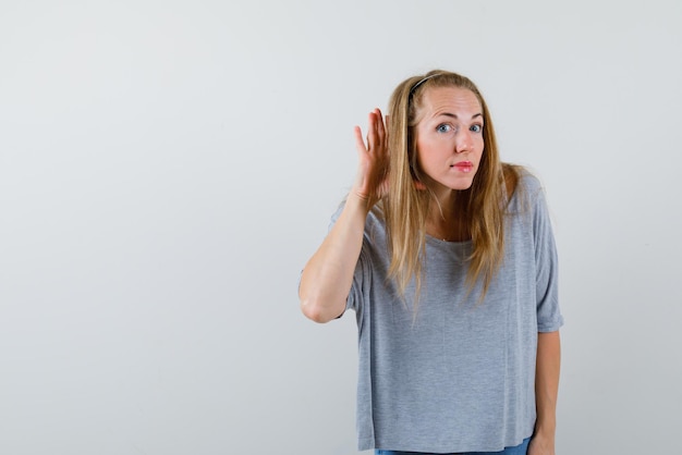 La femme surprise essaie d'entendre en tenant sa main derrière l'oreille sur fond blanc