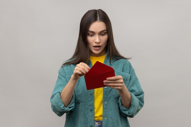 Femme surprise étonnée tenant une enveloppe romantique rouge et regardant une lettre avec la bouche ouverte