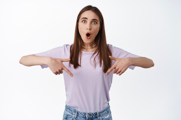 Une femme surprise et impressionnée dit wow pointant vers le bas et regarde étonnée par une publicité montrant une fonctionnalité impressionnante nouveau produit en stock fond blanc