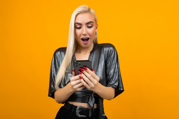 Femme surprise lit les messages sur son smartphone sur un fond de studio jaune