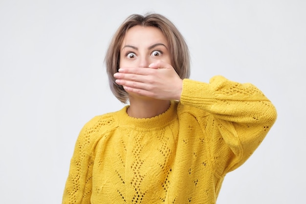 Femme surprise en pull jaune couvrant la bouche avec la main et regardant la caméra