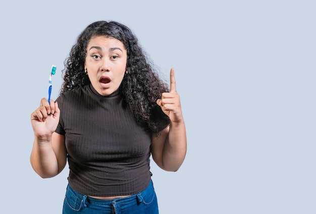 Une femme surprise tenant une brosse à dents pointant vers le haut Une fille étonnée tenant une brossière à dents et pointantvers le haut