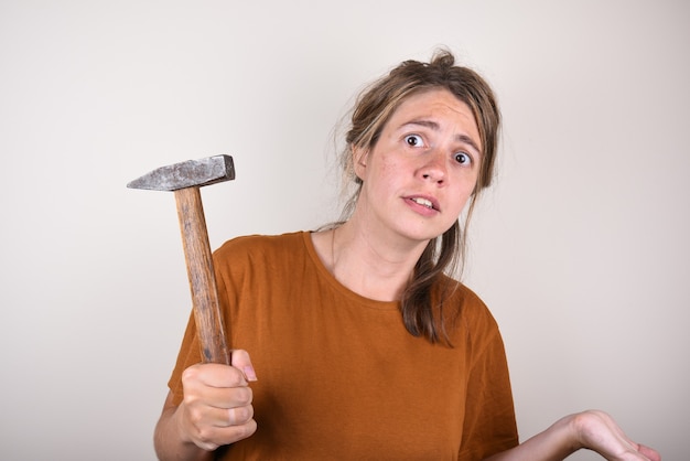 Photo femme surprise tenant un marteau dans ses mains, qui ne sait pas comment faire des réparations dans la maison. la femme avec un marteau est surprise par la question.