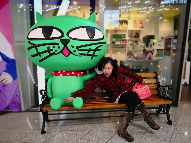 Photo une femme surprise touchant un gros jouet alors qu'elle est assise sur un banc contre le magasin