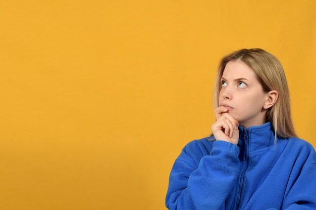 Une femme en sweat-shirt bleu se tient devant un fond jaune