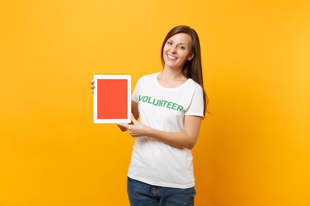 Femme en t-shirt blanc écrit inscription verte titre volontaire tenir tablet pc ordinateur, écran vide vide isolé sur fond jaune. Aide d'assistance gratuite volontaire, concept de travail de grâce de charité.