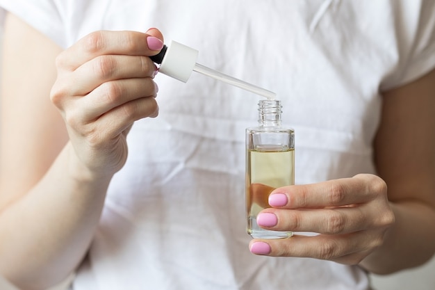 Femme en t-shirt blanc tenant une bouteille d'huile cosmétique, concept de soins de la peau. Photo de haute qualité