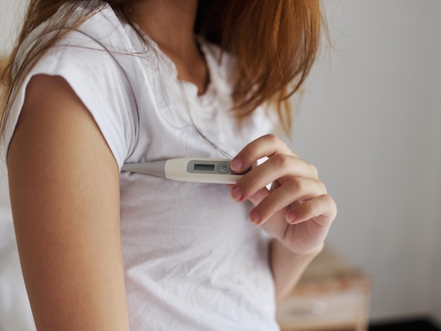 Photo une femme en t-shirt blanc vérifie la température avec un thermomètre sous son bras photo de haute qualité