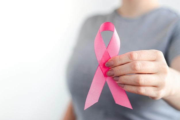 Femme en t-shirt gris tenant un ruban rose dans ses mains Mois de sensibilisation au cancer du sein Soutenir et promouvoir la campagne contre le cancer Concept de soins de santé Copier l'espace