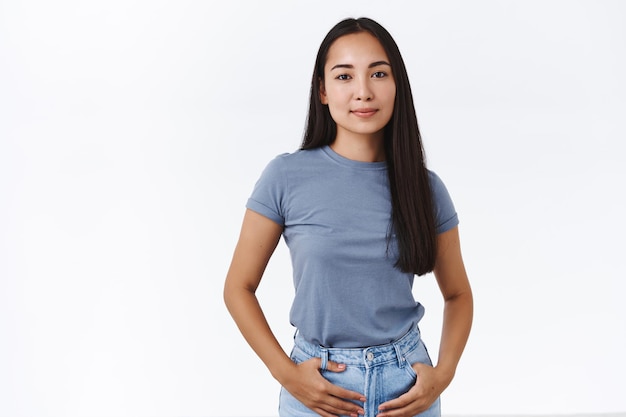 femme en t-shirt, jeans, tenir les mains dans les poches, pose confiante, souriante heureuse