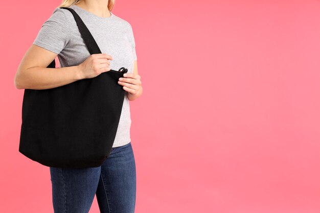 Femme en t-shirt avec sac noir sur fond rose