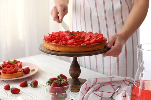 Une femme en tablier a coupé la tarte aux fraises.