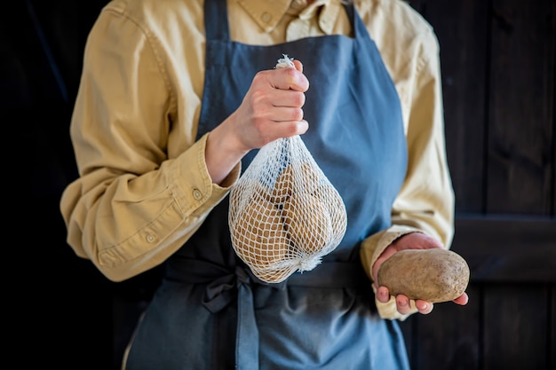 Femme en tablier détient des pommes de terre dans le panier