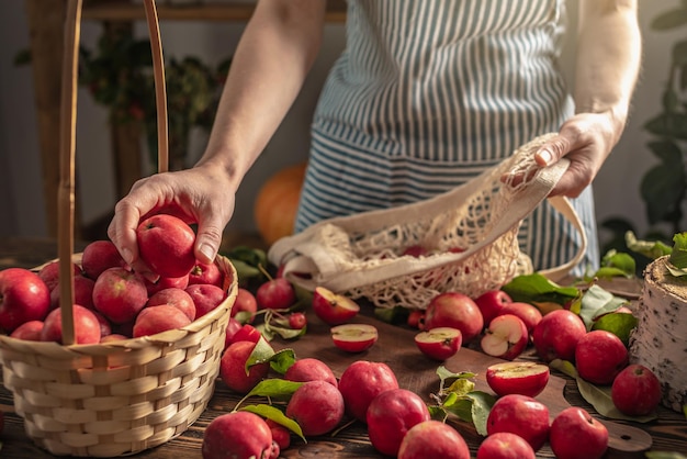 Femme en tablier met des pommes rouges fraîches d'une table en bois dans la cuisine dans un sac à cordes Concept de récolte de cuisine et d'atmosphère chaleureuse d'automne