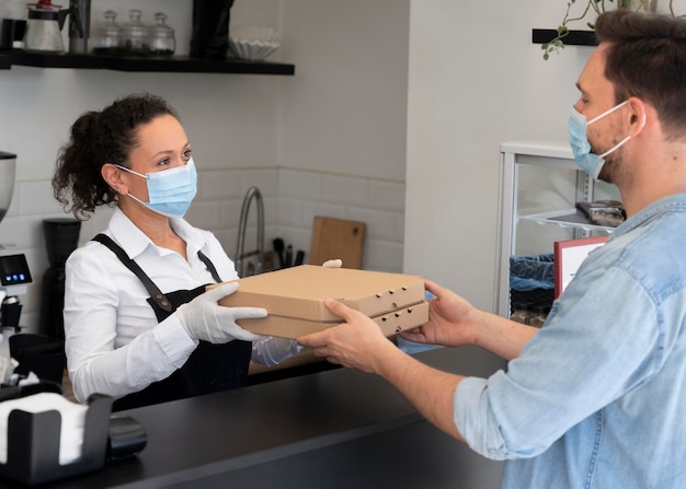 Femme avec tablier offrant des plats à emporter emballés à un client masculin