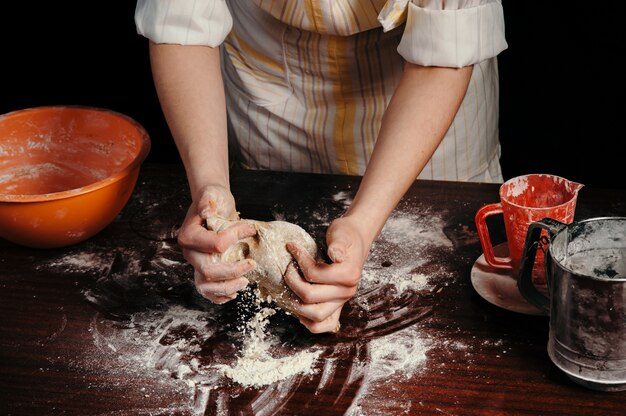 Femme en tablier pétrit la pâte sur la vieille table en bois