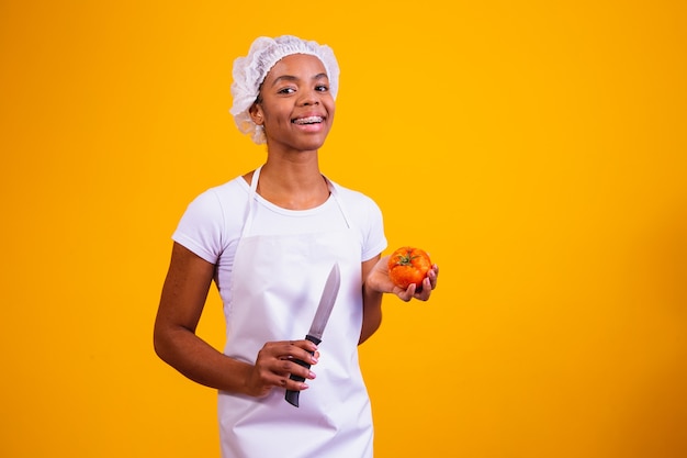 Femme en tablier tenant un couteau et une tomate.